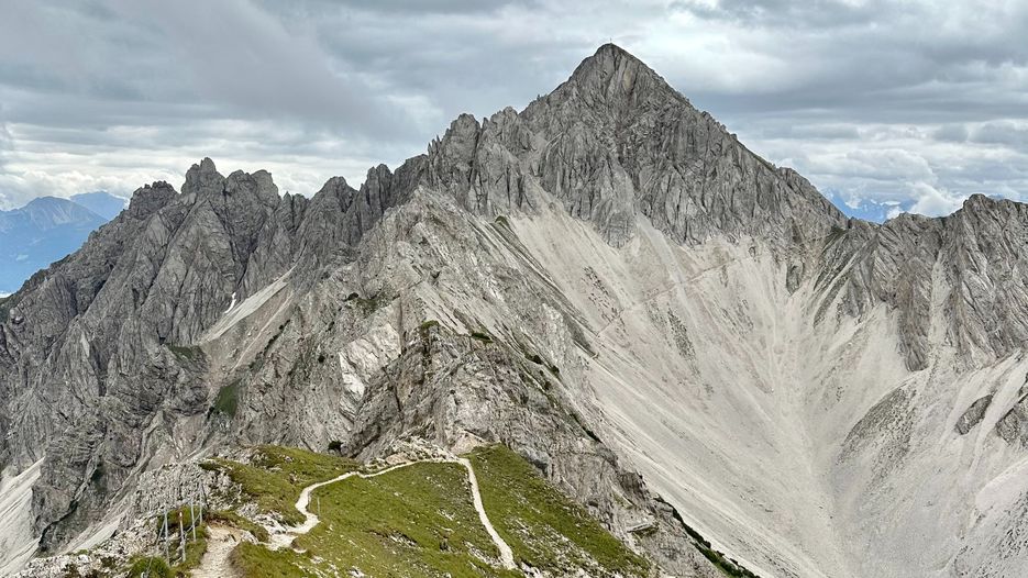 Eine beeindruckende Berglandschaft mit schroffen Gipfeln und einem Wanderweg, der sich durch die alpine Umgebung schlängelt.