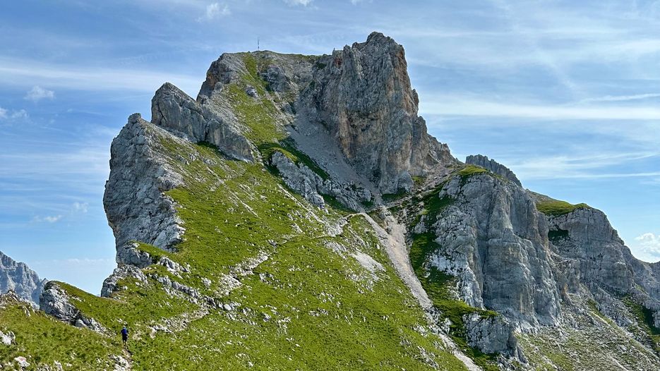 Eine beeindruckende Berglandschaft mit steilen Felsen und grünem Gras, unter blauem Himmel mit einigen Wolken.