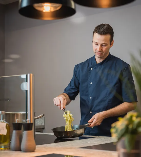 Chef in navy uniform cooking pasta in modern kitchen under pendant lights
