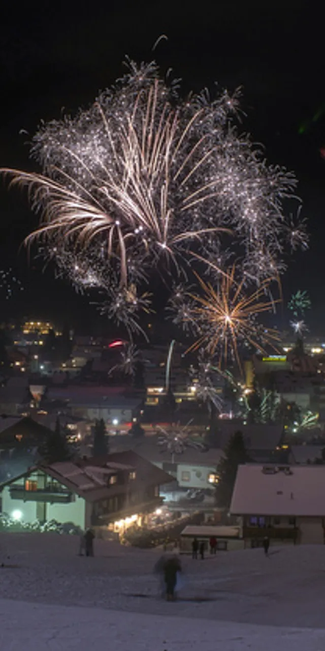 Bunte Feuerwerke erhellen den Nachthimmel über einem verschneiten Alpendorf
