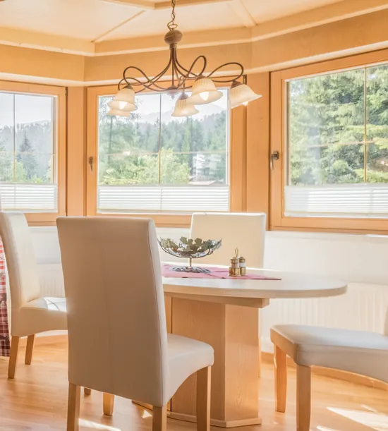 Gemütliches Wohnzimmer im Alpendesign mit grauem Sofa, Holzdecke und hellem Essbereich