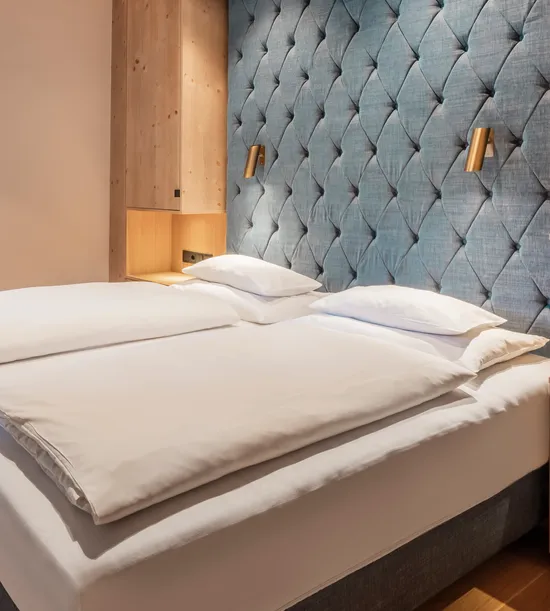 Modernes Hotelzimmer mit Doppelbett, Holzakzenten und gepolsterter blauer Wandverkleidung
