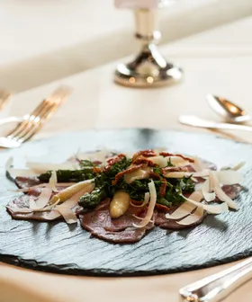 Gourmet-Rinder-Carpaccio mit Parmesanspänen, Spargel und getrockneten Tomaten auf schwarzem Schiefer