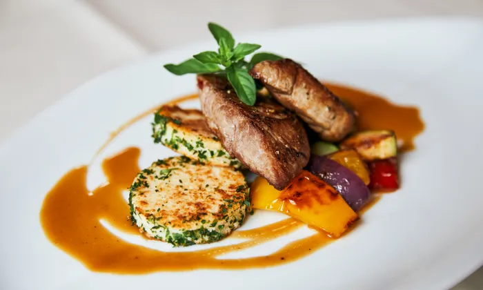 Grilled lamb medallions with herb-crusted potato cakes and roasted vegetables on brown sauce