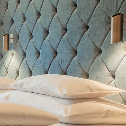 Modernes Hotelbett mit weißen Kissen und gepolstertem blauen Kopfteil mit integrierten Leselampen