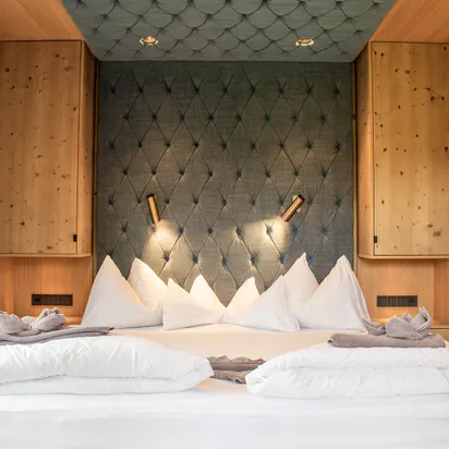 Modern hotel bed with white pillows, blue tufted headboard, and wooden accents