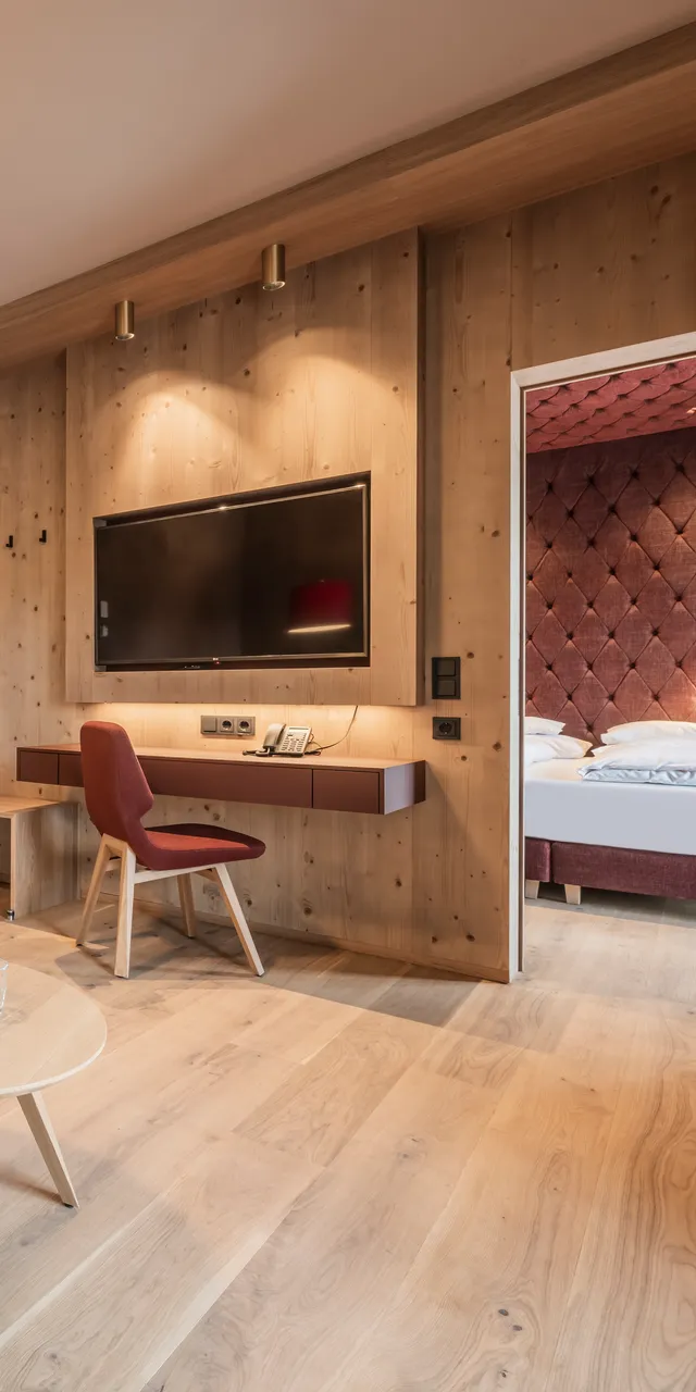 Modern hotel suite with wooden interior, red furniture, flat-screen TV and connected bedroom