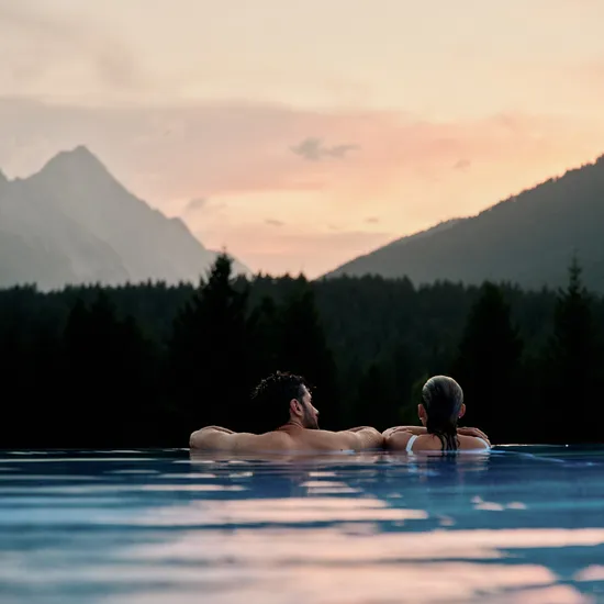 Paar entspannt im Infinity-Pool mit Bergblick bei Sonnenuntergang