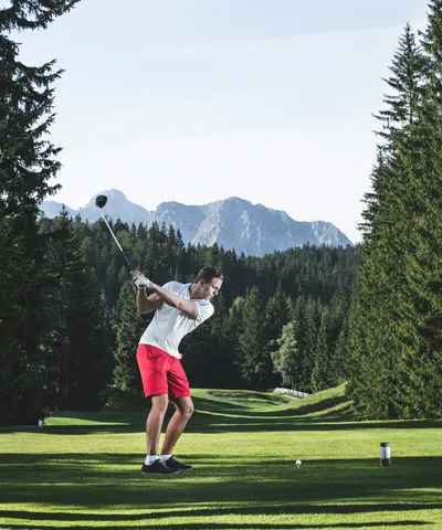 Golfer in red shorts swinging a golf club on a scenic mountain course