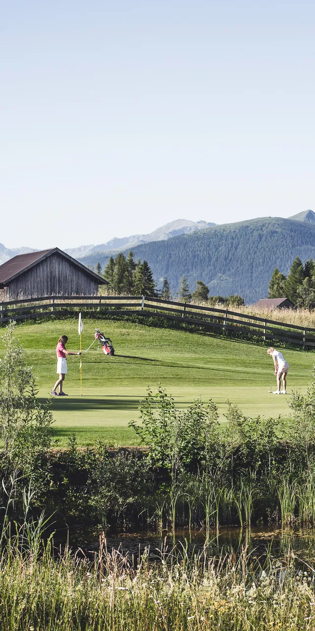 Zwei Golfspieler auf einem malerischen Golfplatz in den Bergen, umgeben von Bäumen und Holzzaun