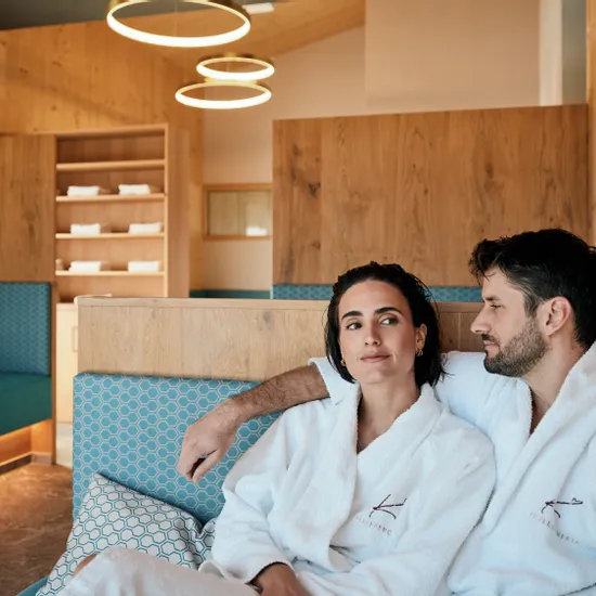 Paar entspannt in Spa-Lounge in weißen Bademänteln mit Wellness-Logo