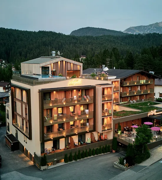 Modern alpine hotel with balconies and rooftop terrace surrounded by mountains and forest