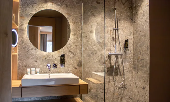 Modern bathroom with stone walls, round mirror, sink, and walk-in glass shower