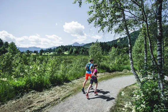 Two trail runners on a forest path with scenic mountain landscape in summer