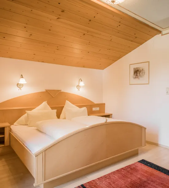 Cozy hotel room with sloped wooden ceiling, double bed, and warm lighting