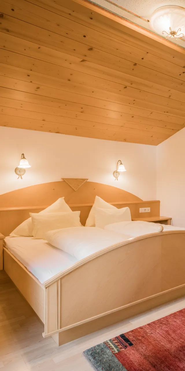 Gemütliches Hotelzimmer mit schräger Holzdecke, Doppelbett und warmem Licht