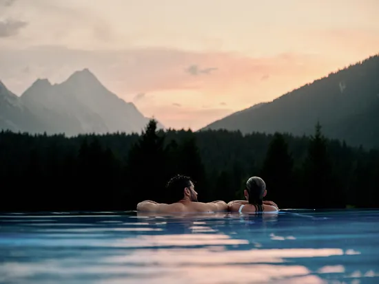 Couple relaxing in an outdoor infinity pool with mountain views at sunset