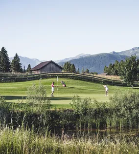 Zwei Golfspieler auf einem malerischen Golfplatz in den Bergen, umgeben von Bäumen und Holzzaun