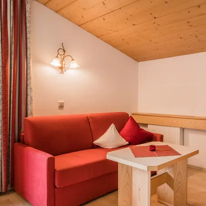 Gemütliche Hotelecke mit rotem Sofa, Sessel, Holztisch und schräger Holzdecke