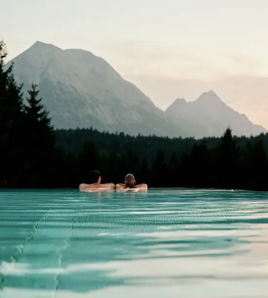 Paar entspannt im Infinity-Pool mit malerischem Bergblick bei Sonnenuntergang