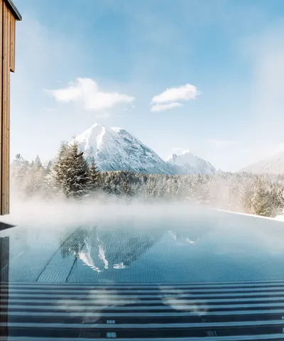 Dampf steigt aus Infinity-Pool mit Blick auf schneebedeckte Alpenberge auf