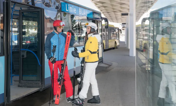 Skifahrer mit Ausrüstung am Skibus-Halt Linie BLAU im Wintersportort