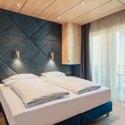 Modern hotel room with double bed, wood paneling, balcony and geometric headboard
