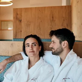Paar entspannt in Spa-Lounge in weißen Bademänteln mit Wellness-Logo