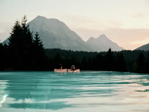 Couple relaxing in infinity pool with scenic mountain view at sunset