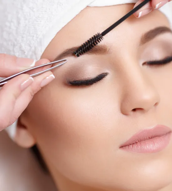 Woman receiving eyebrow shaping with tweezers and brush at beauty salon