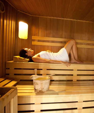 Frau entspannt auf Holzbank in einer warm beleuchteten finnischen Sauna