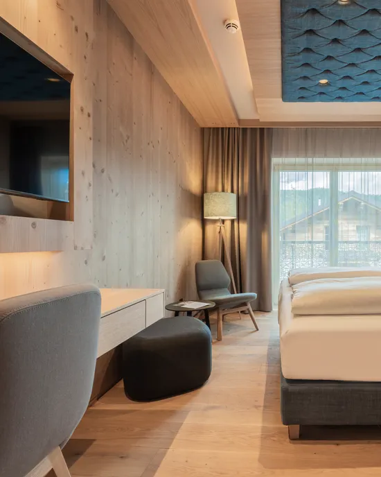 Modern hotel room with wooden furniture, large bed, and quilted blue wall panels
