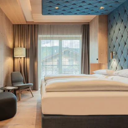 Modernes Hotelzimmer mit Holzmöbeln, großem Bett und gesteppten blauen Wandpaneelen