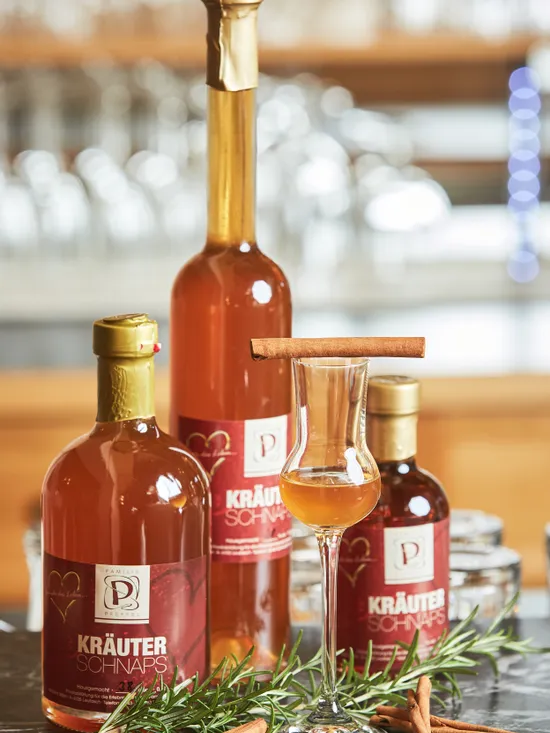 Flaschen Kräuterschnaps mit gefülltem Glas, Zimtstangen und Rosmarin auf dunkler Oberfläche