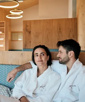 Couple relaxing in spa lounge wearing white robes with wellness logo