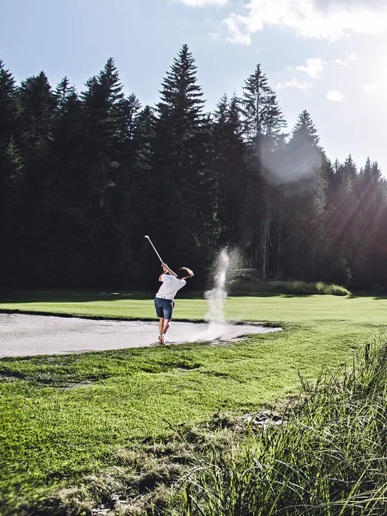 Golfers playing on a scenic mountain golf course with pond and pine trees