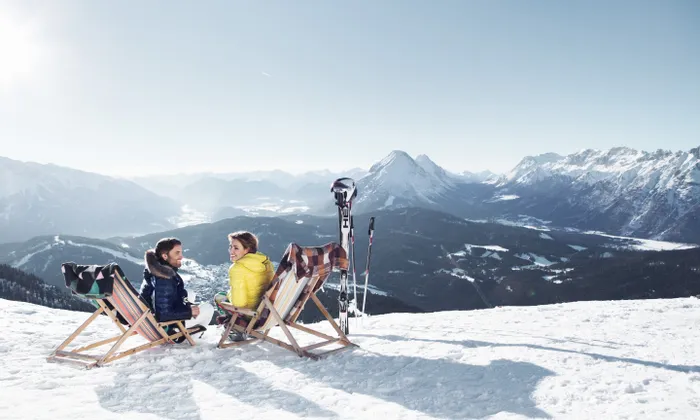 Couple relaxing on deck chairs in snowy Alps with ski gear and mountain panorama