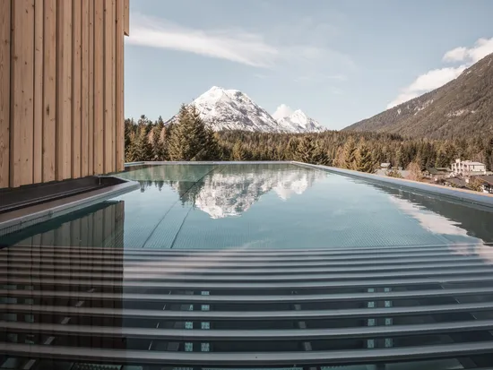 Infinity-Pool mit Bergblick und Nadelwald unter klarem blauen Himmel