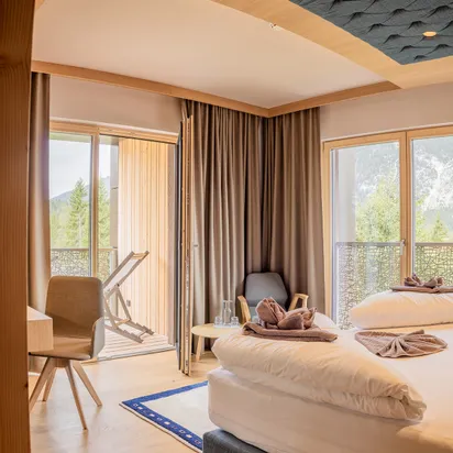 Gemütliches Hotelzimmer mit Doppelbett, Balkonmöbeln und Bergblick durch große Fenster