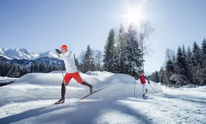 Zwei Personen beim Langlaufen an einem sonnigen Wintertag in verschneiter Berglandschaft