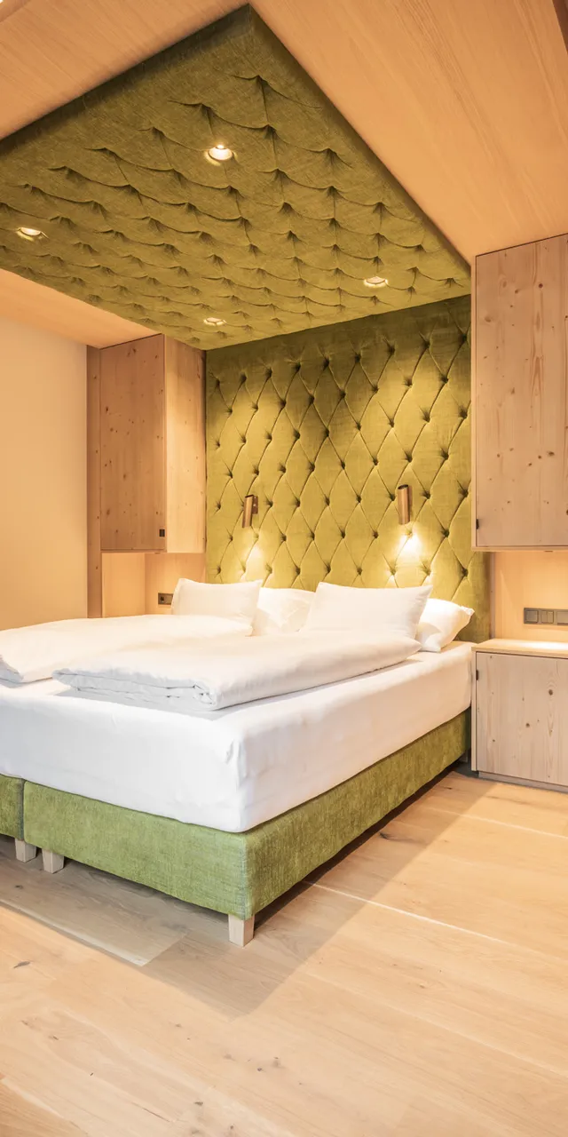 Modernes Hotelzimmer mit grünem Polsterbett, Holzmöbeln und gemütlicher Beleuchtung