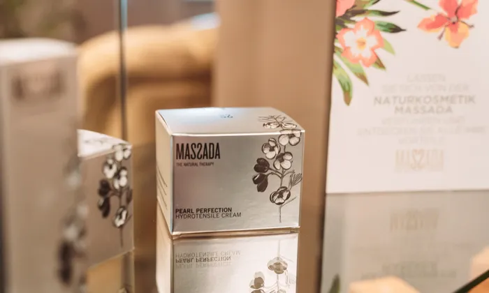 Massada Pearl Perfection Creme-Schachtel auf Glasfläche mit floralem Produktaufsteller