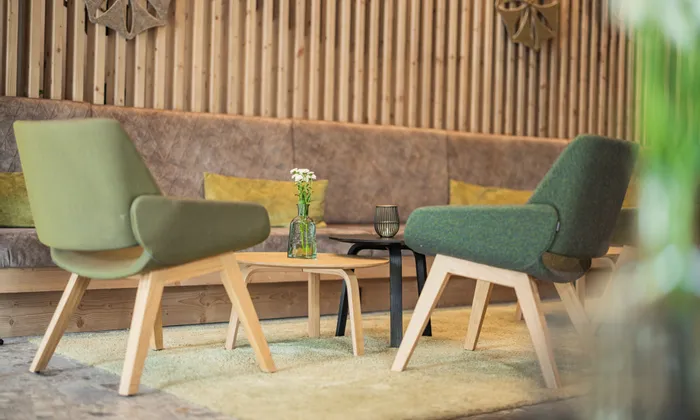 Modern lounge area with green armchairs, wood tables, and flower vase on beige rug