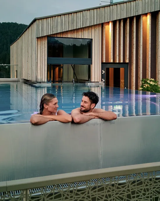 Paar entspannt im Infinity-Pool auf dem Dach eines luxuriösen Alpinresorts mit Holzarchitektur