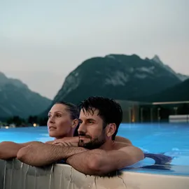Couple relaxing in rooftop infinity pool with mountain view at dusk