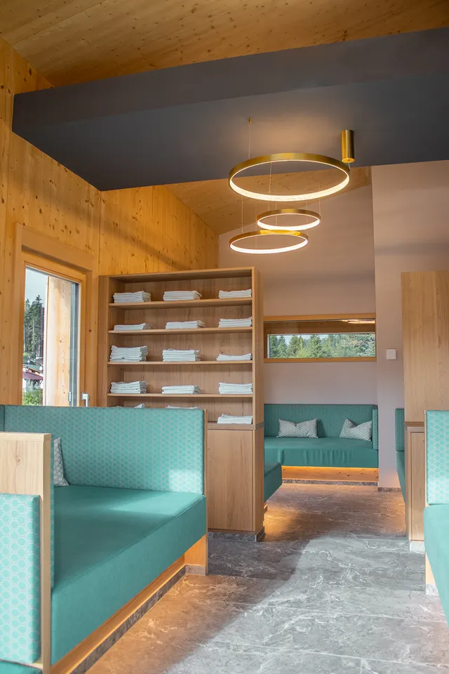 Moderner Spa-Loungebereich mit Holzwänden, türkisfarbenen Sitzbänken, Handtuchregal und runden Deckenlampen