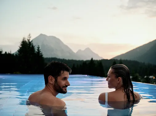 Couple relaxing in infinity pool with mountain view at sunset