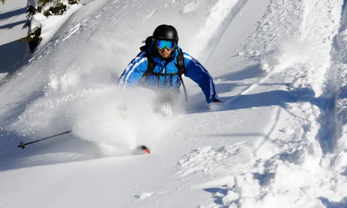Skier in blue jacket gliding through deep powder snow on a sunny mountain slope