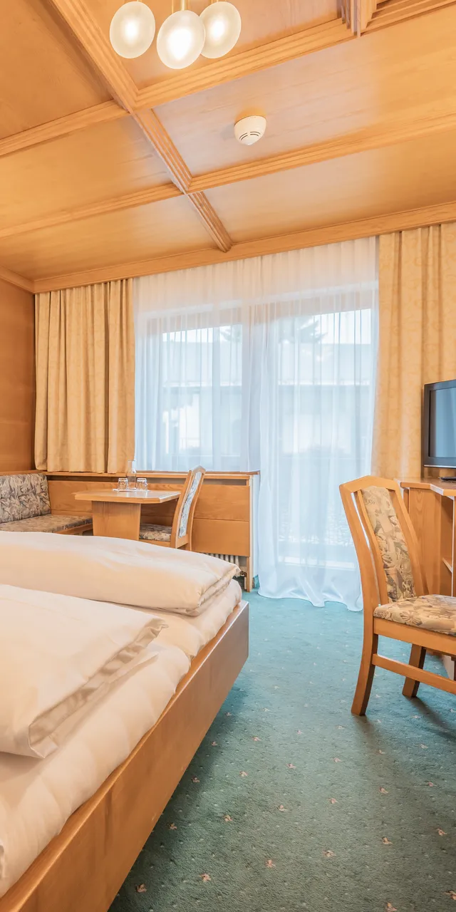 Gemütliches Hotelzimmer mit Doppelbett, Holzmöbeln, Schreibtisch, Fernseher und Balkonzugang