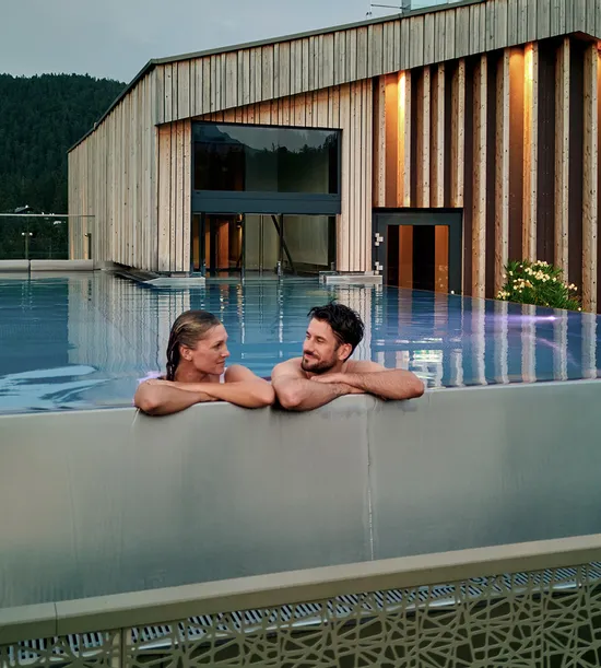 Paar entspannt im Infinity-Pool auf dem Dach eines luxuriösen Alpinresorts mit Holzarchitektur